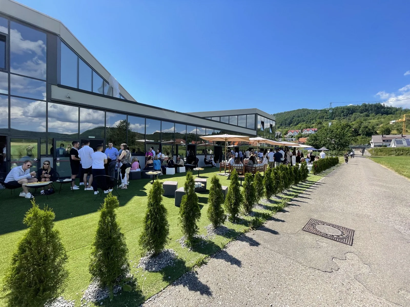Firmensommerfest auf Außenterrasse mit Glasfassade, Sonnenschirmen und Rasenfläche — AchtWerk Catering